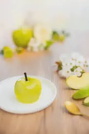 Green apple trompe-l'œil pastry on a white plate, styled with apple slices and blossom