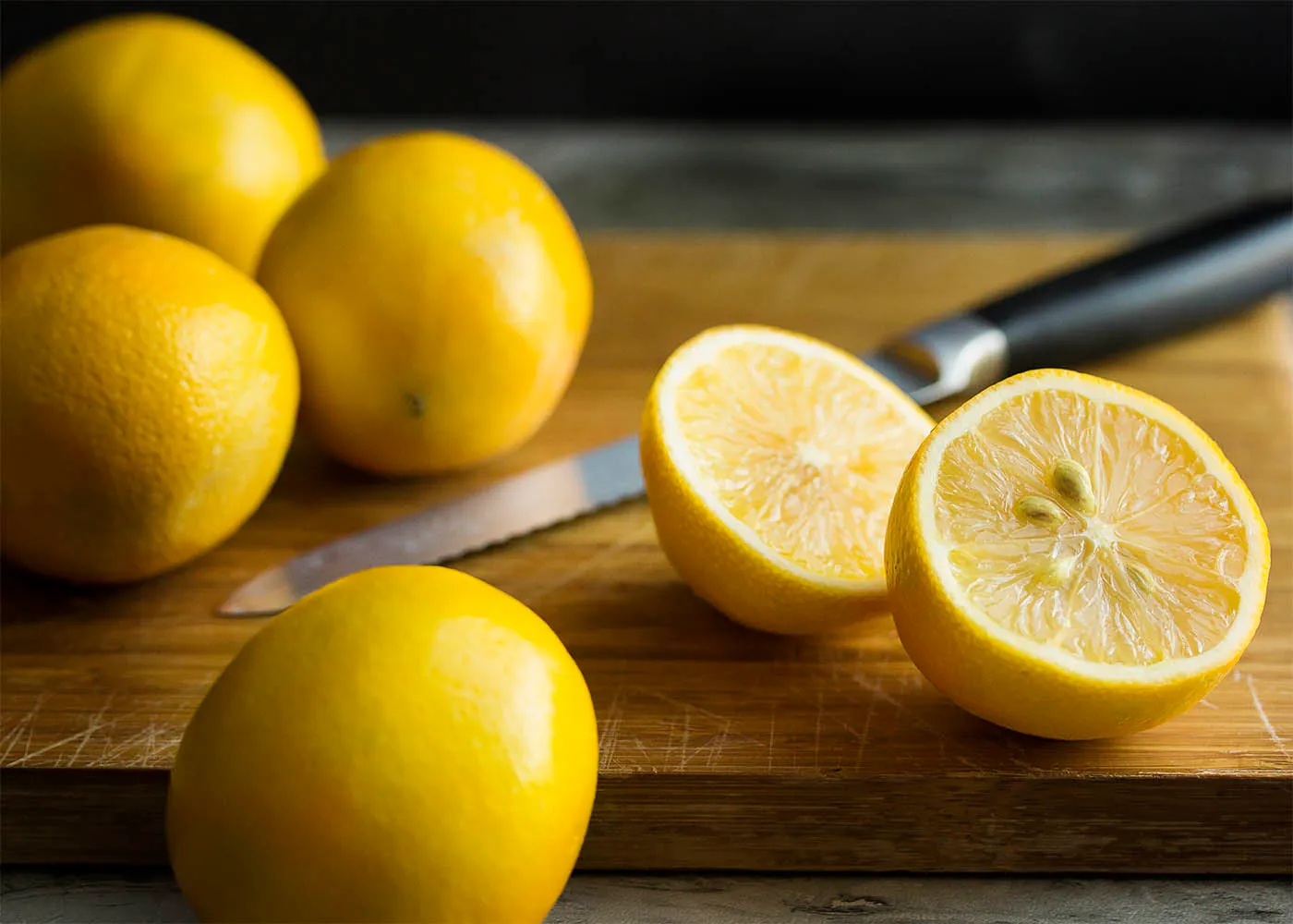 Meyer lemons on a wooden cutting board with a knife and a single cut lemon