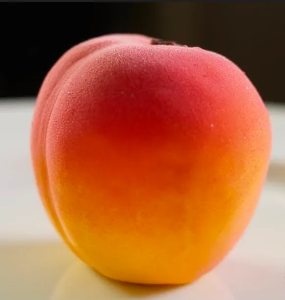 Close-up of a peach trompe-l'œil entremets, blush-to-gold velvet finish indistinguishable from real fruit
