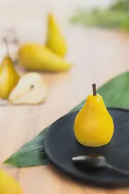 Yellow pear trompe-l'œil pastry on a black plate, styled with a pear leaf